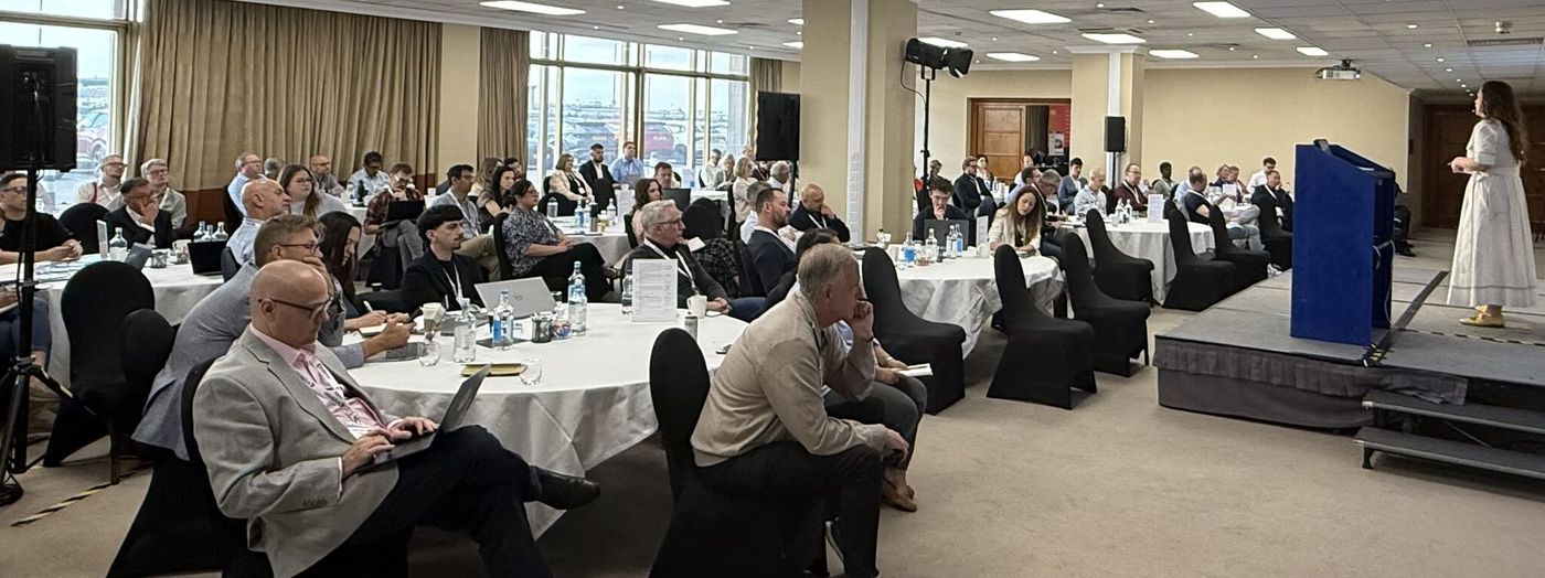 A full conference room at a past CEdMA Enterprise conference, with members at round tables listening to a speaker